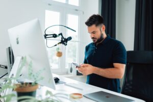 An influencer sat at a desk with video recording equipment whilst on their phone