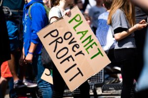 People holding a hand-painted sign at a protest reading 'PLANET over PROFIT'