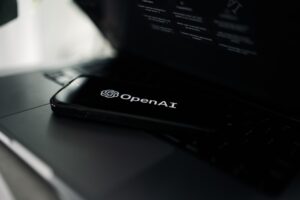 OpenAI company logo in white letters on a black phone resting on a black laptop